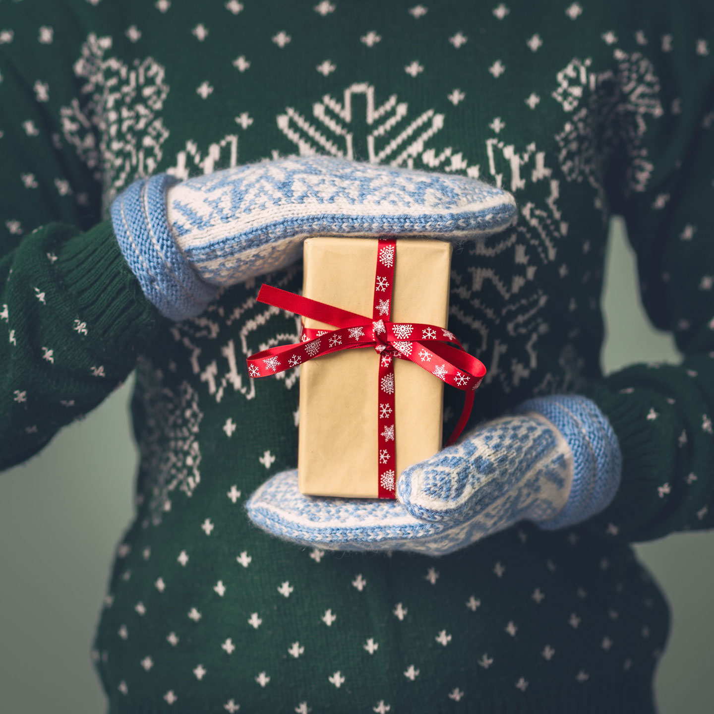 Hands in mittens holding a holiday gift